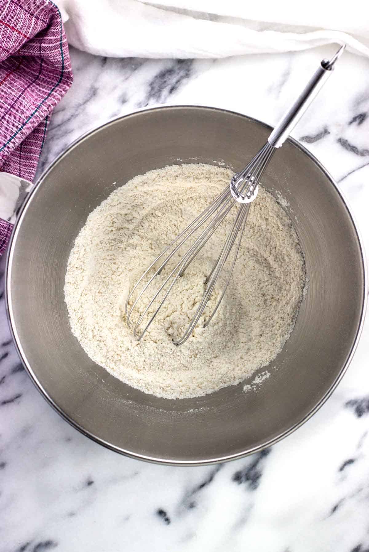 Some flour, yeast, salt, and sugar whisked together in a stand mixer bowl.