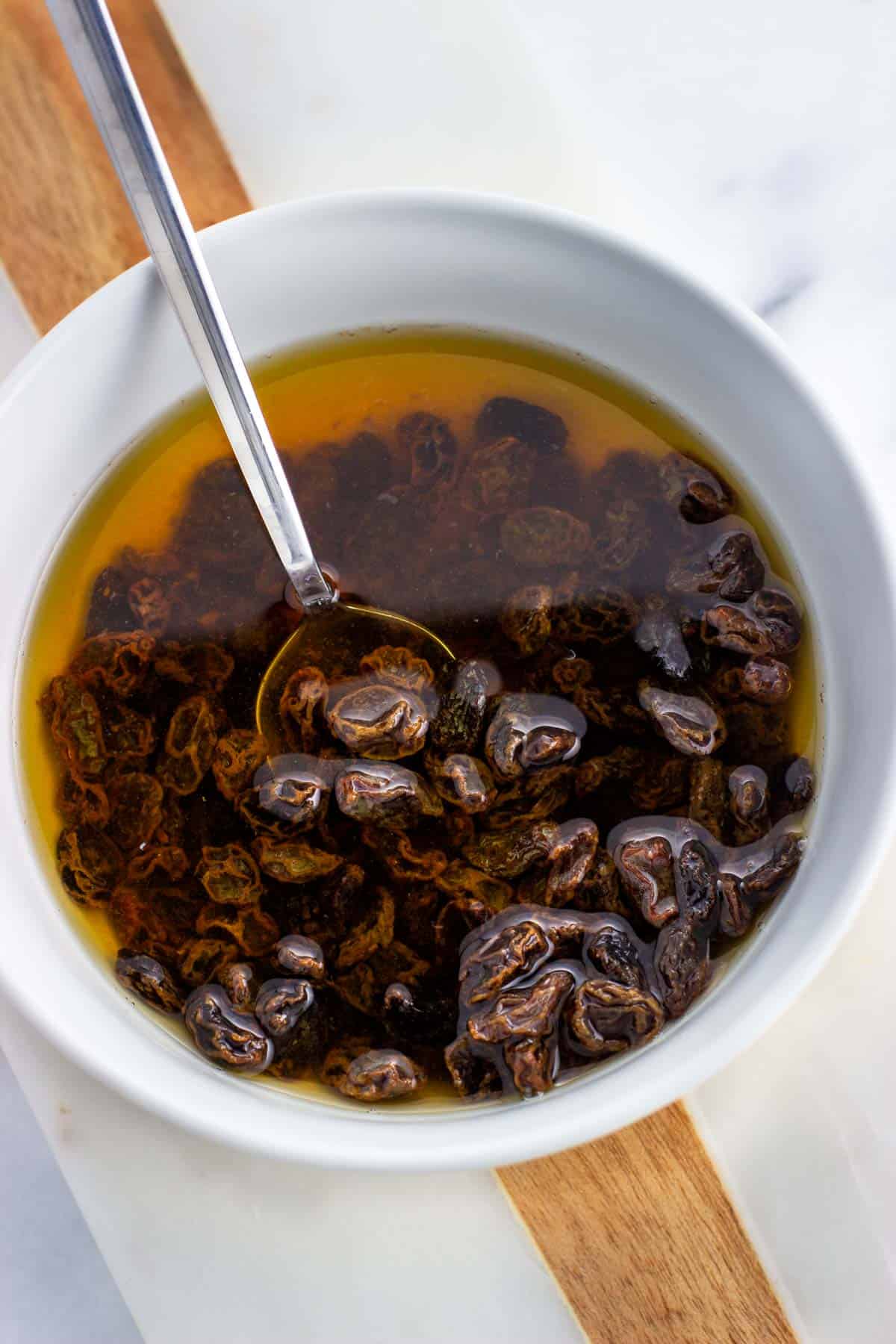 A bowl of raisins soaking in water and brown sugar.