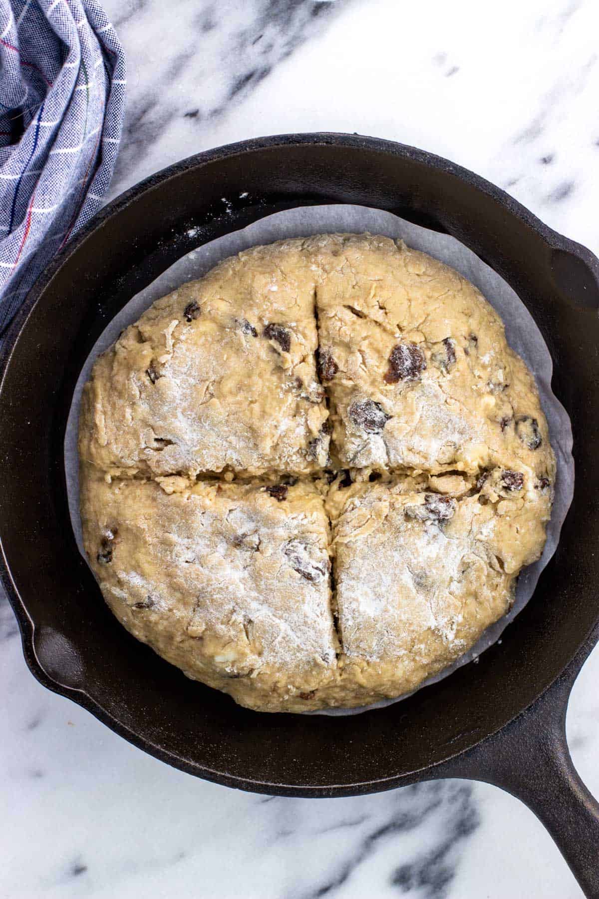 Irish soda bread dough with a cross cut into the top transferred to a cast iron skillet.