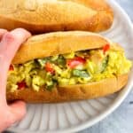 A hand holding a pepper and egg sandwich on a plate.