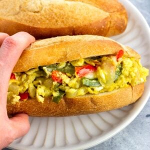 A hand holding a pepper and egg sandwich on a plate.