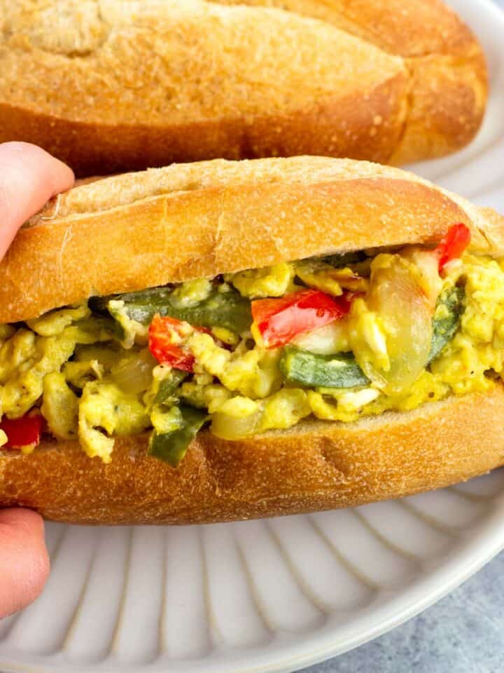 A hand holding a pepper and egg sandwich on a plate.