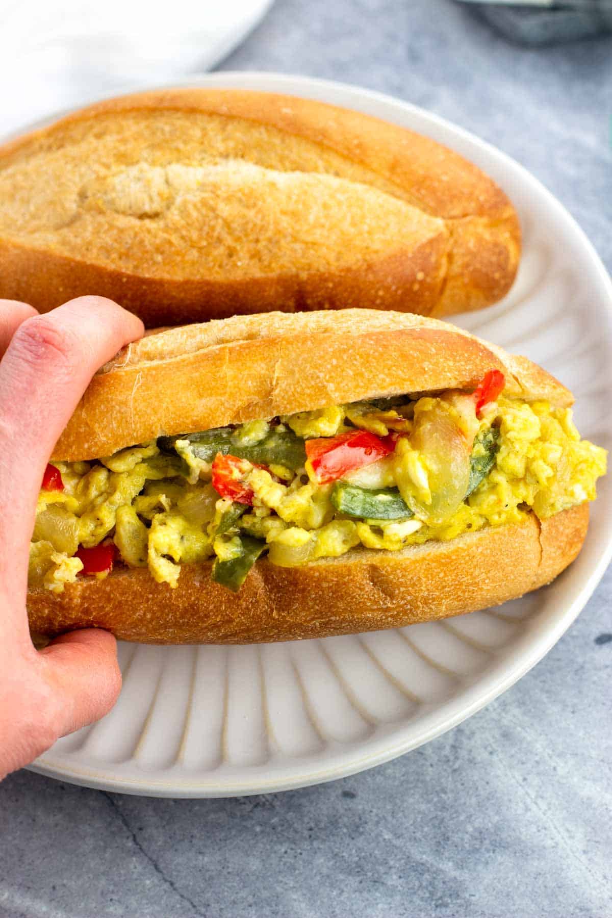 A hand holding a pepper and egg sandwich on a plate.