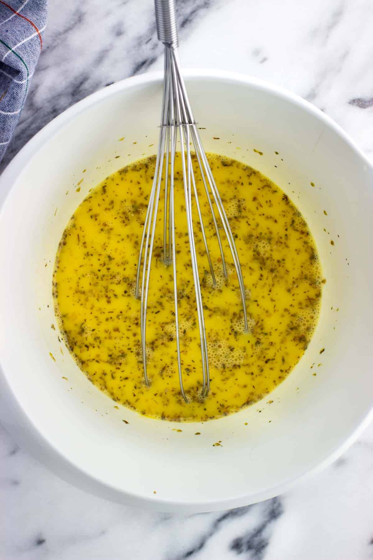 Beaten eggs, milk, and spices in a bowl with a whisk.