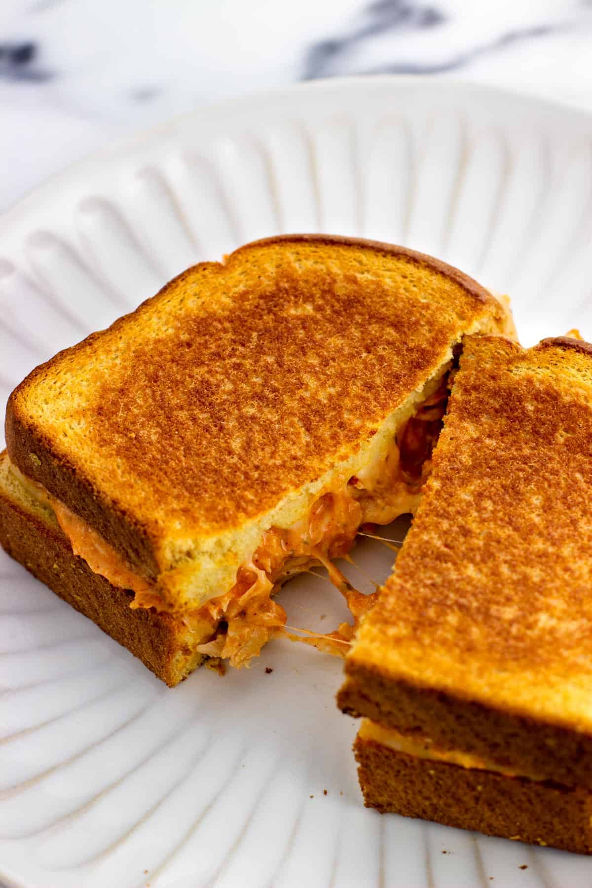 A buffalo chicken grilled cheese cut in half with cheese stretched between.