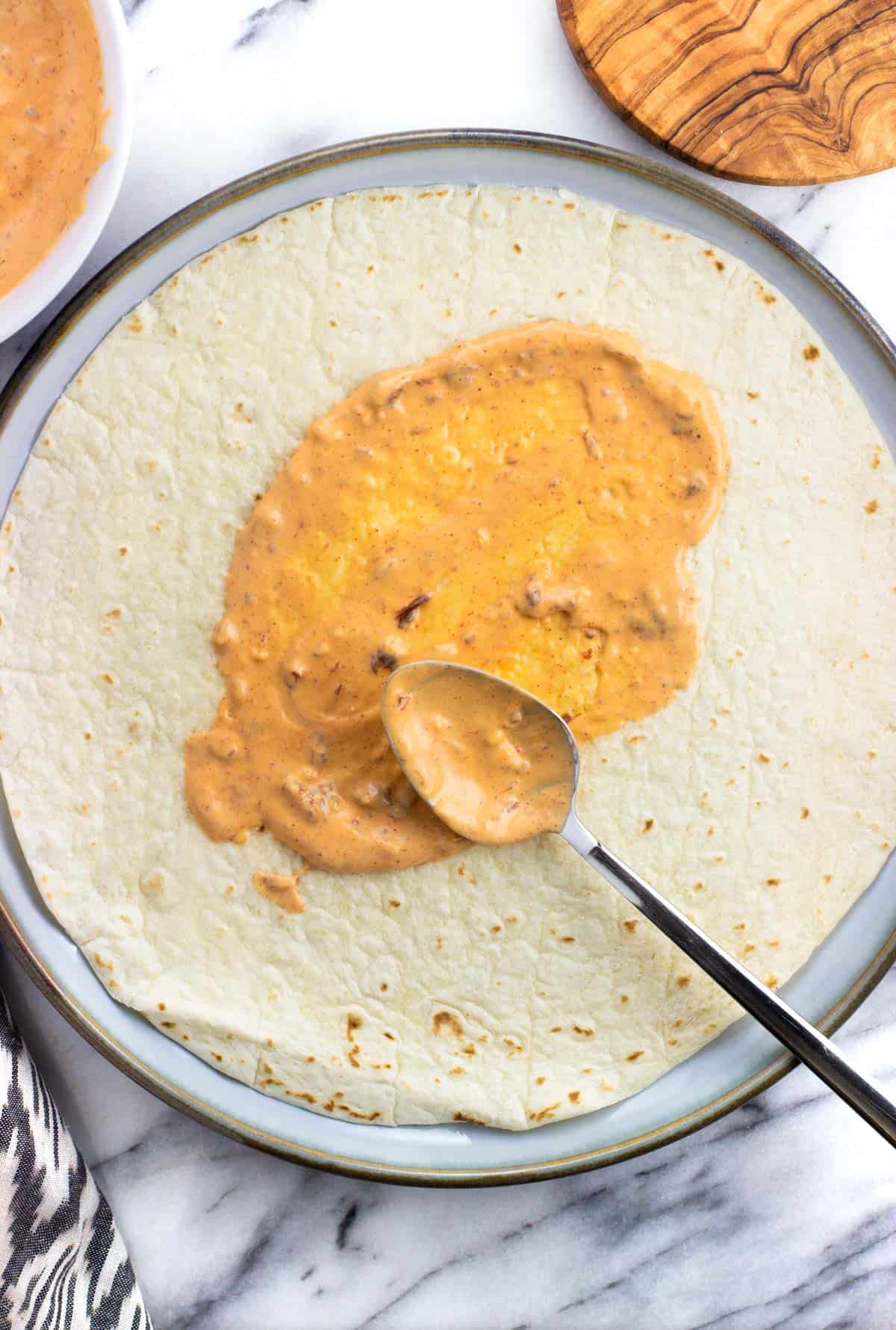 Aioli being spread along a tortilla with a spoon.
