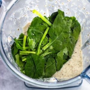 Frozen spinach leaves added to a smoothie in a blender.