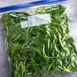 Spinach leaves packed into a gallon plastic bag with the air pressed out.