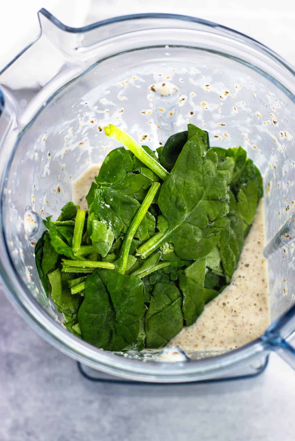 Frozen spinach leaves added to a smoothie in a blender.