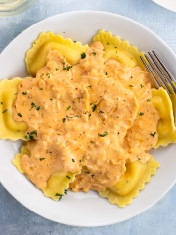 A bowl of lobster ravioli topped with a cream sauce with a fork.