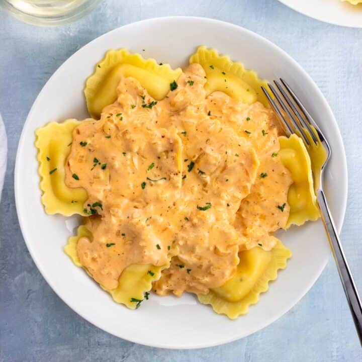 A bowl of lobster ravioli topped with a cream sauce with a fork.