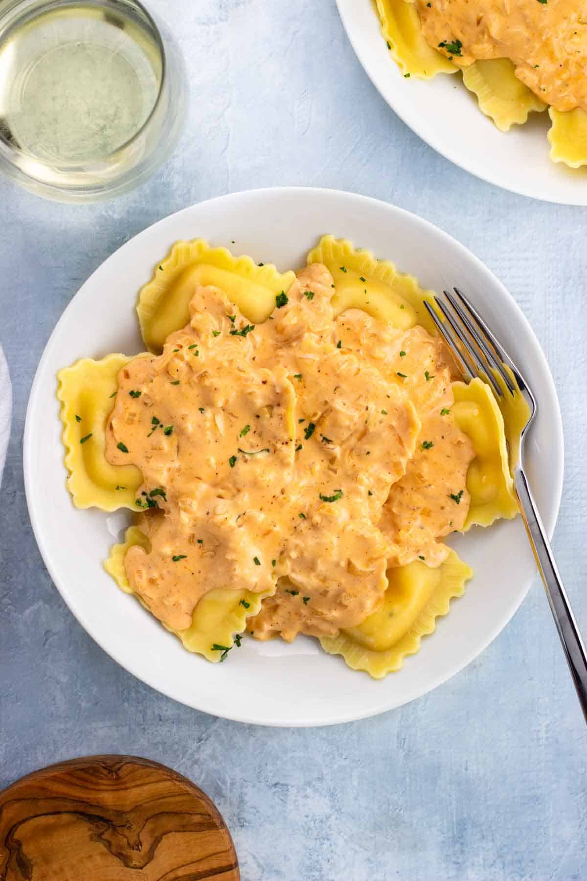 A bowl of lobster ravioli topped with a cream sauce with a fork.