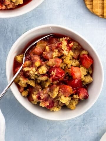 A bowl of strawberry rhubarb crumble with a spoon.