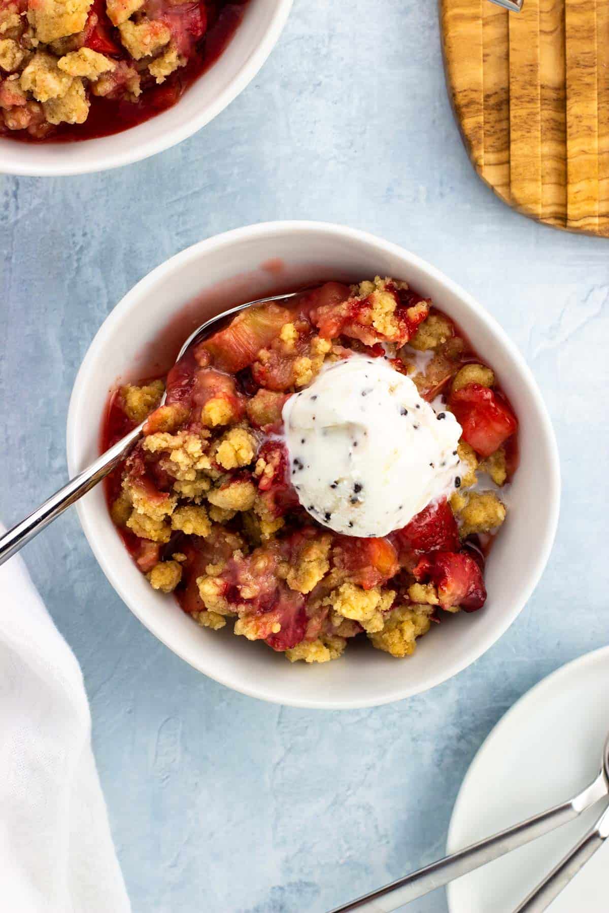 A bowl of strawberry rhubarb crumble topped with ice cream.