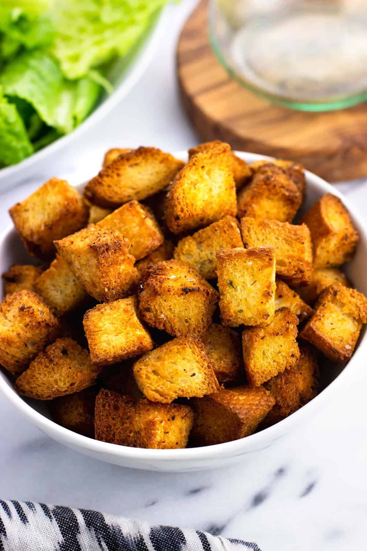 A bowl of croutons with lettuce in the background.