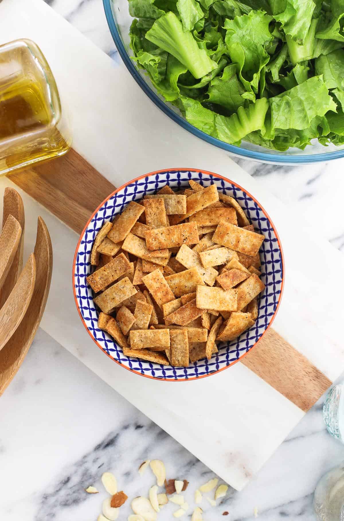 A small bowl of baked tortilla strips surrounded by salad fixings.