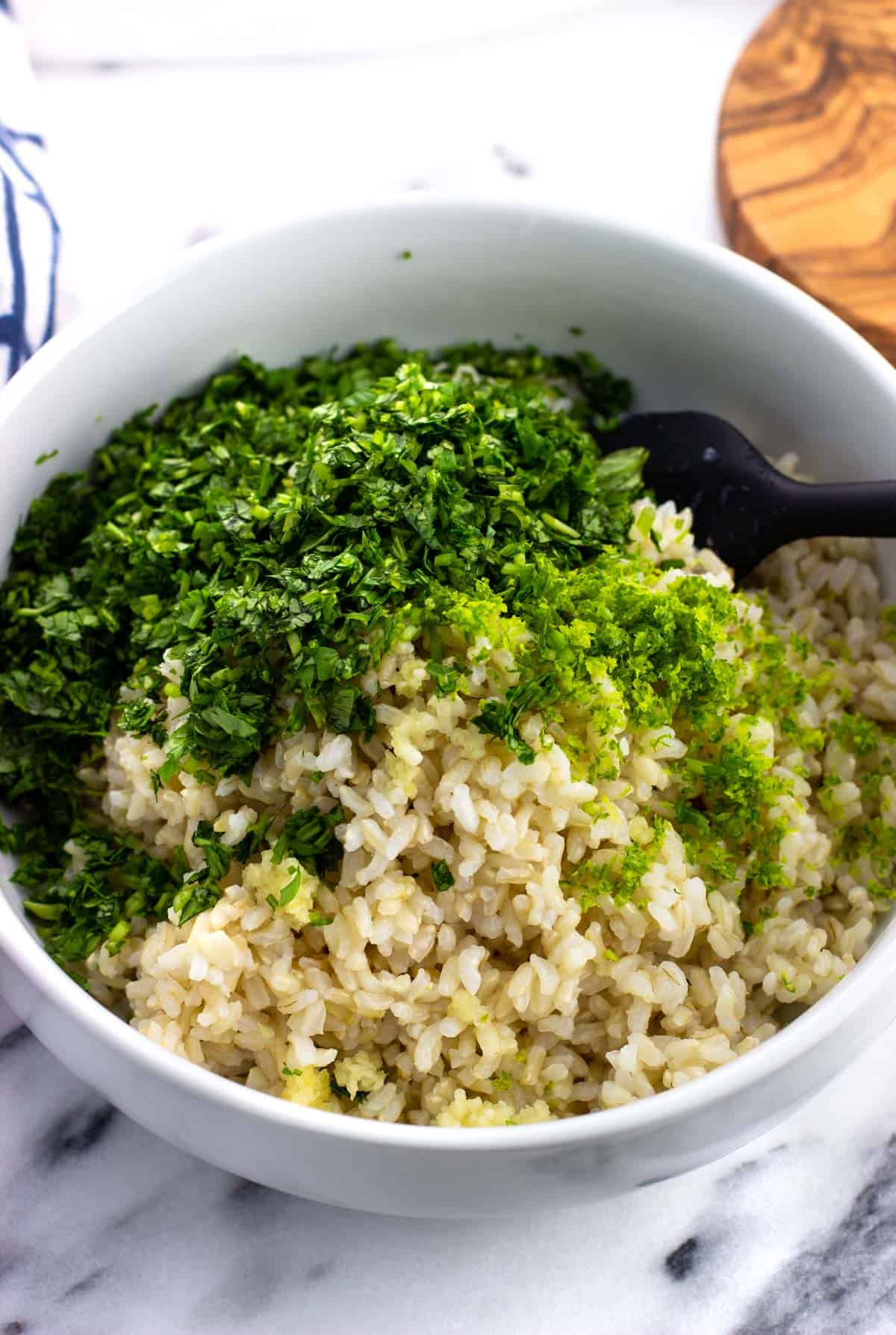 Cooked brown rice and the rest of the ingredients in a bowl before being stirred together.