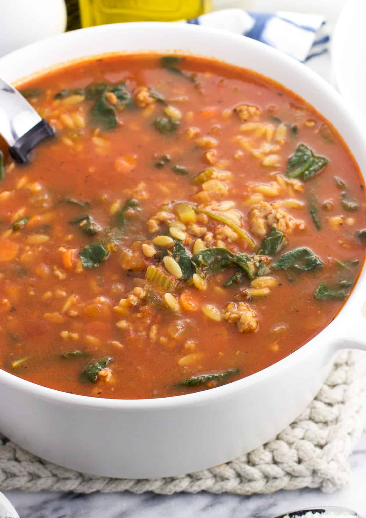 A large pot of Italian sausage soup with a ladle in it.