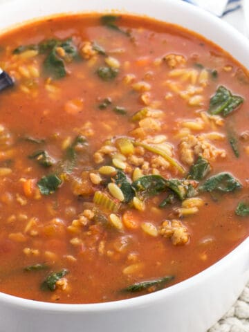 A large pot of Italian sausage soup with a ladle in it.