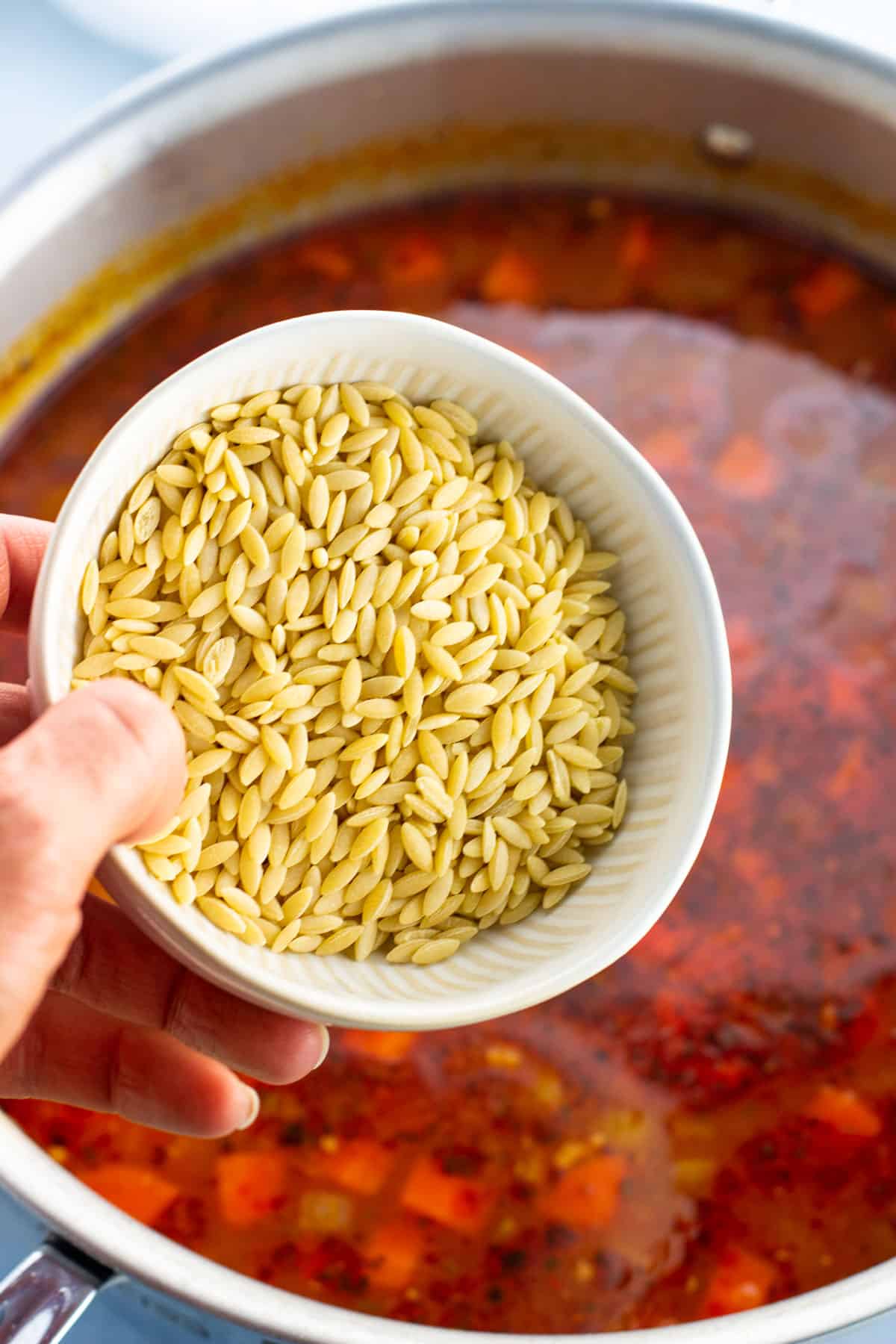 Dry orzo being added to the pot of Italian sausage soup.