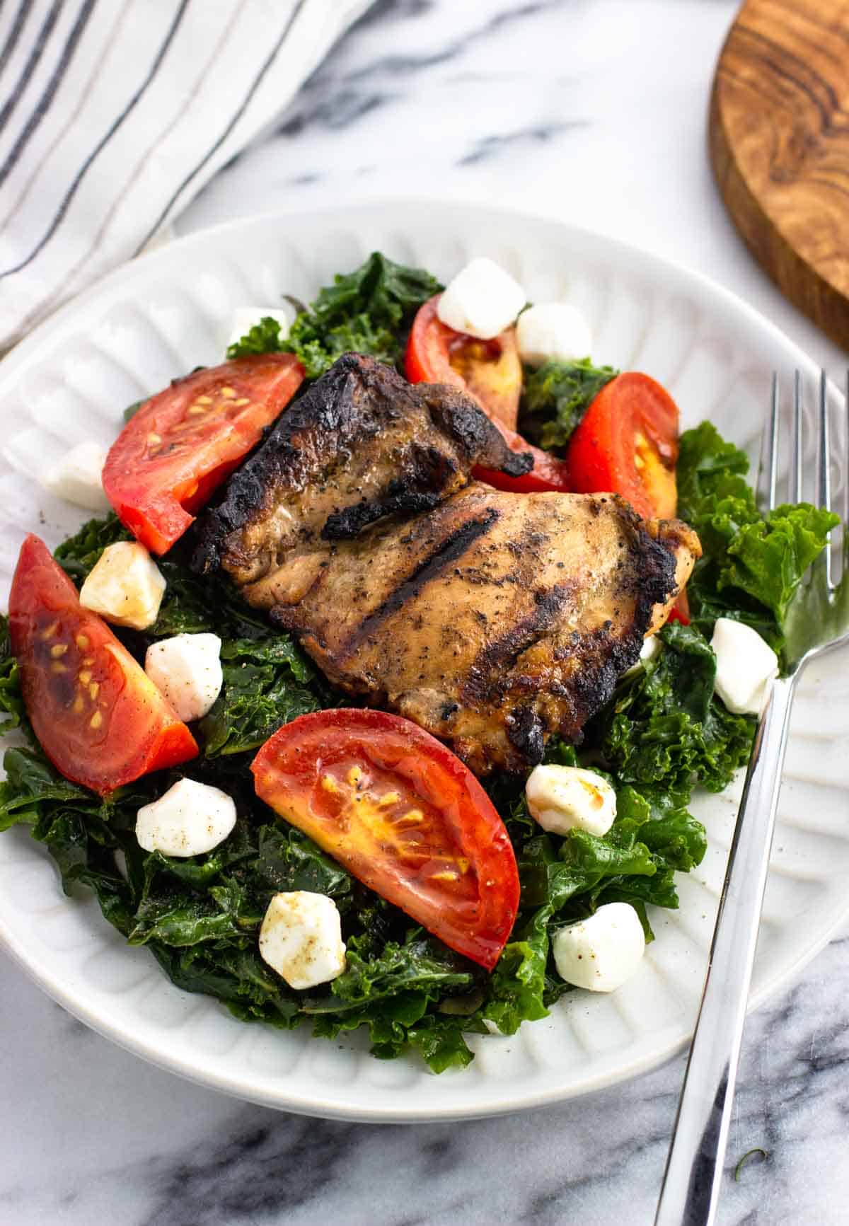 A grilled chicken thigh on marinated kale caprese salad.
