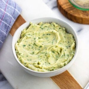 A bowl of roasted garlic butter on a marble board.