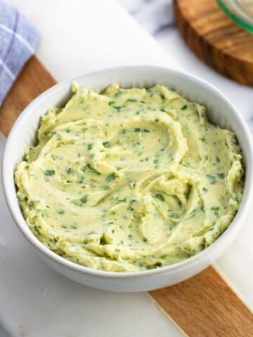 A bowl of roasted garlic butter on a marble board.