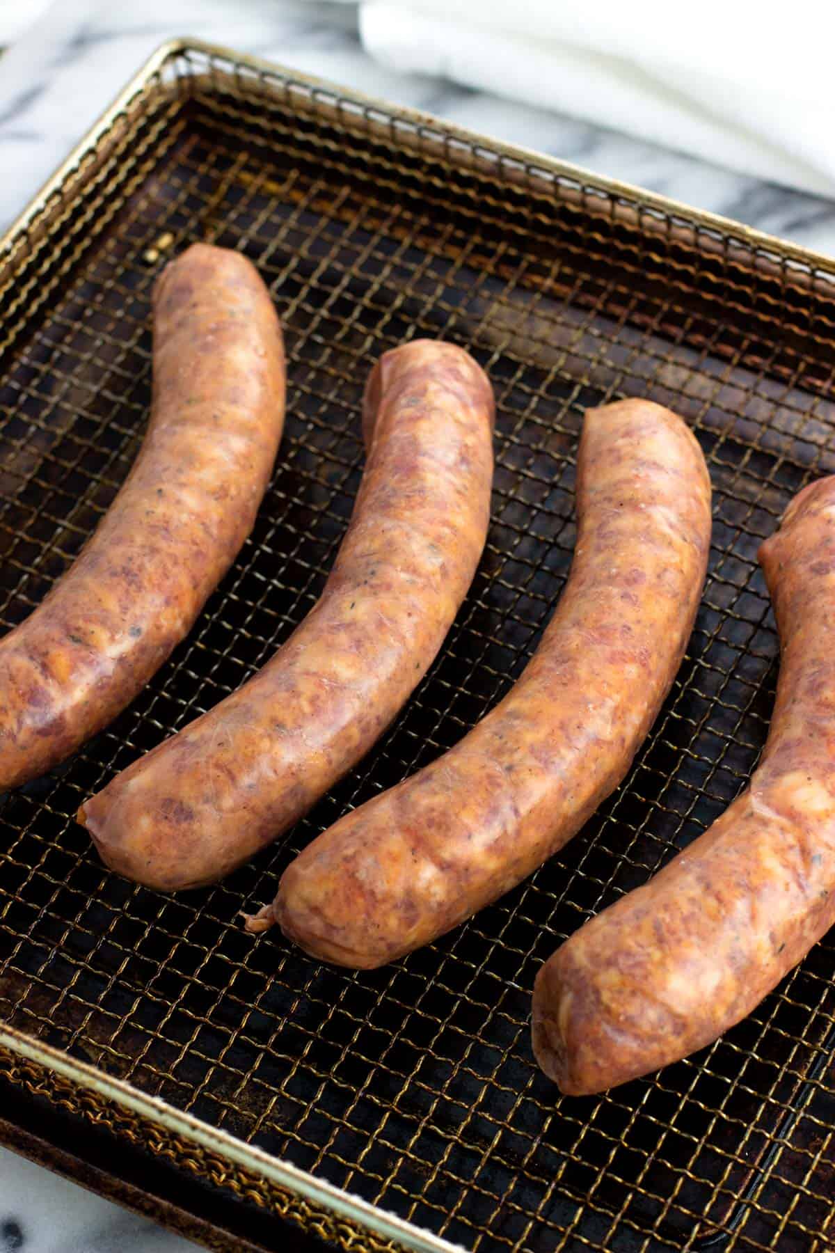 Four raw Italian sausage links on an air fryer basket.