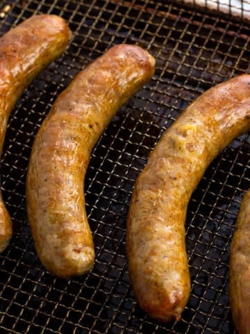 Golden-brown cooked Italian sausages on an air fryer basket.