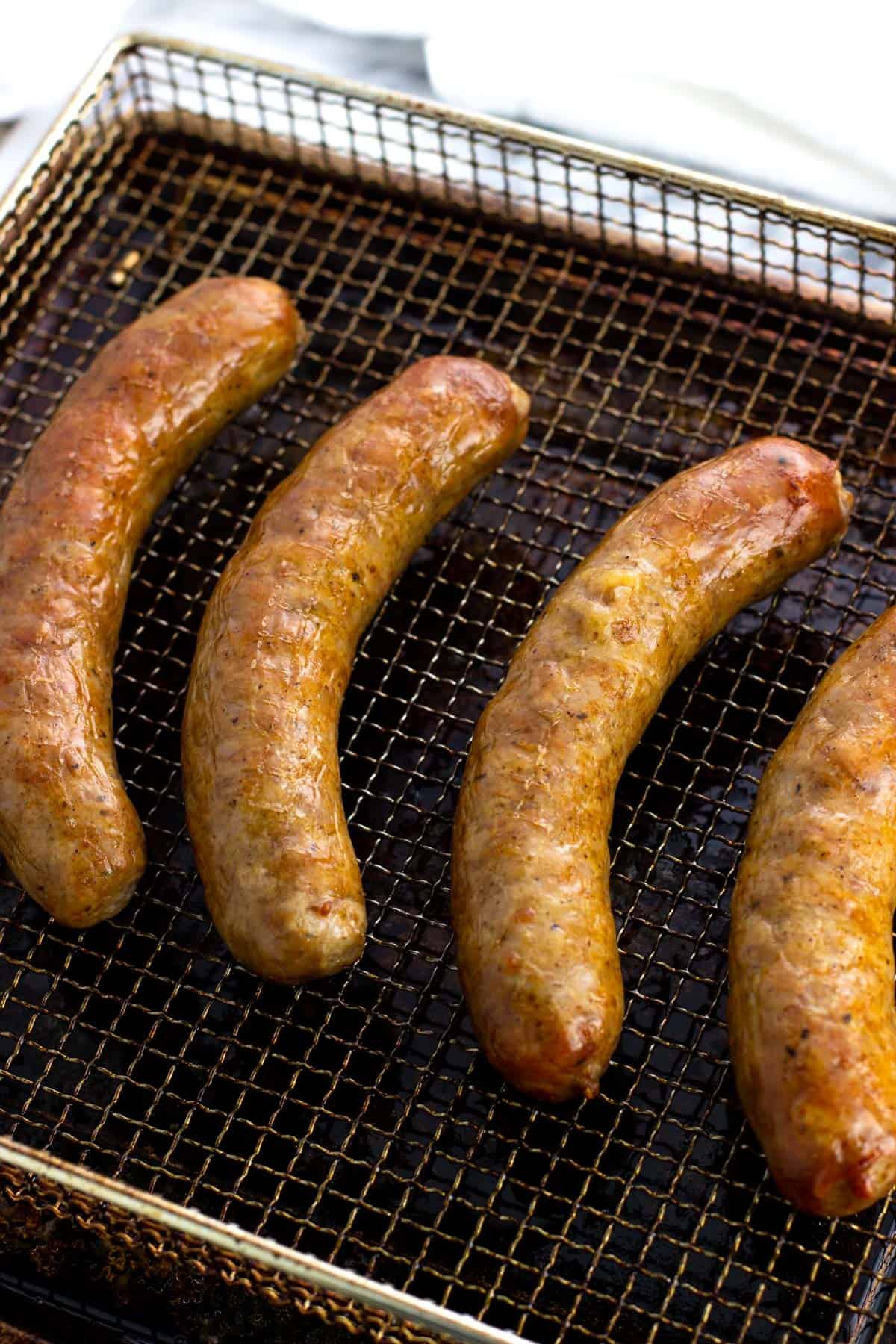 Cooked and browned sausage links on an air fryer basket.