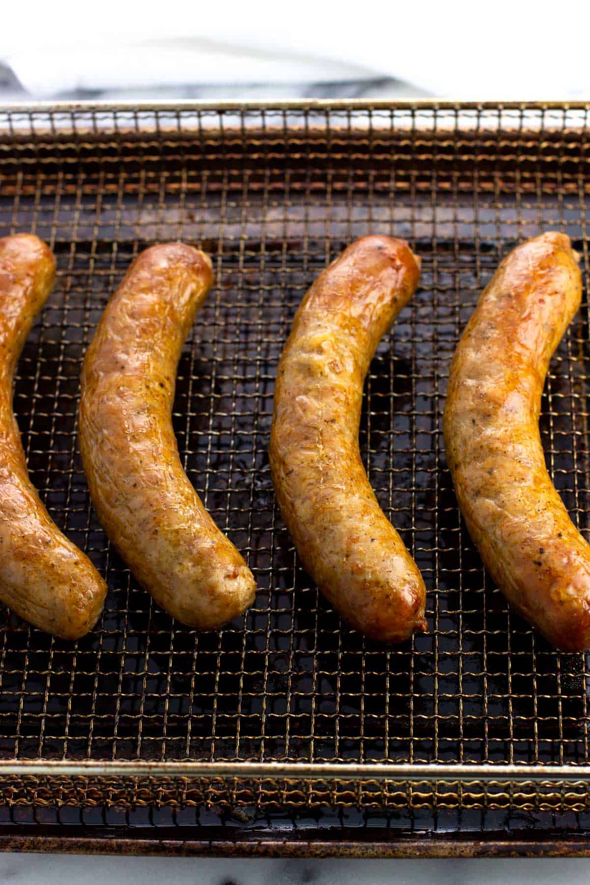 Cooked and browned sausage links on an air fryer basket.