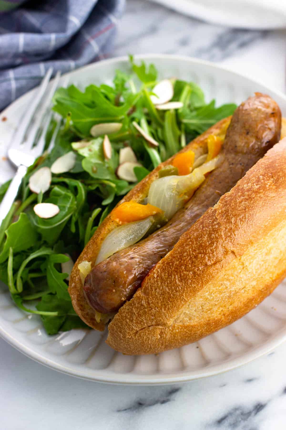 An air fryer sausage in a bun with peppers on a plate with a side salad.