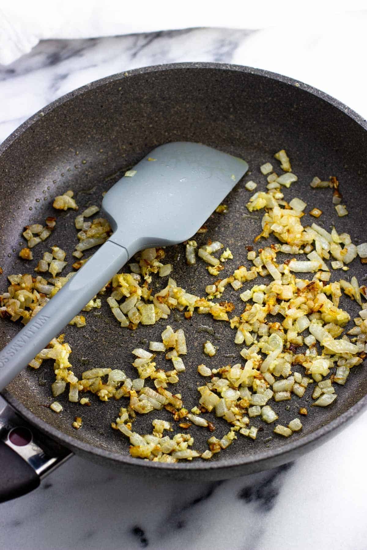 Sautéed onion and garlic in a skillet with a spatula.