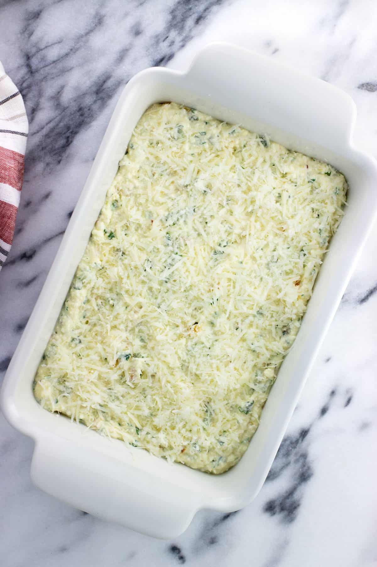 The ricotta mixture in a rectangular dish topped with grated Parmesan before baking.