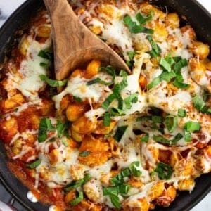 A skillet of chicken Parmesan gnocchi with a wooden serving spoon in it.