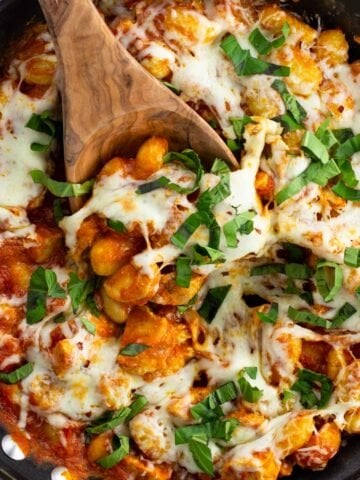 A skillet of chicken Parmesan gnocchi with a wooden serving spoon in it.