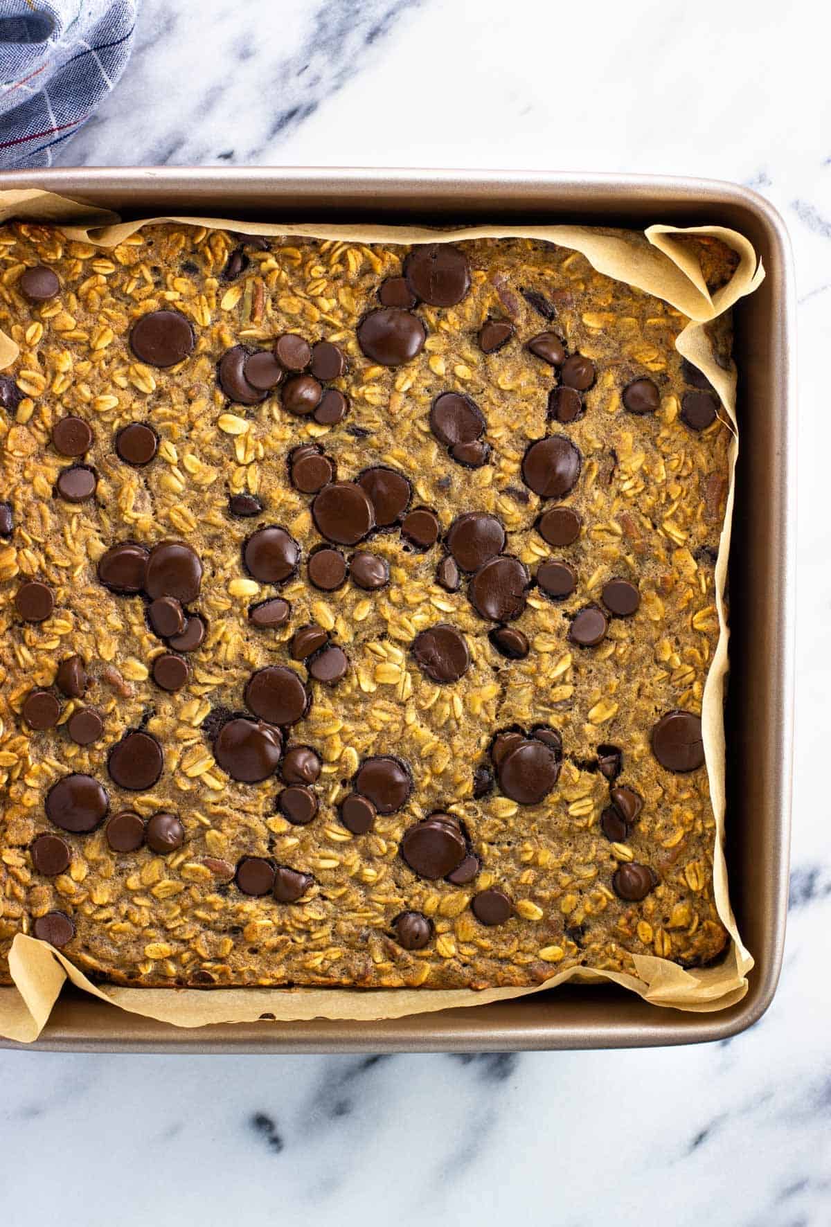 Baked chocolate chip oatmeal in a parchment-lined square pan.