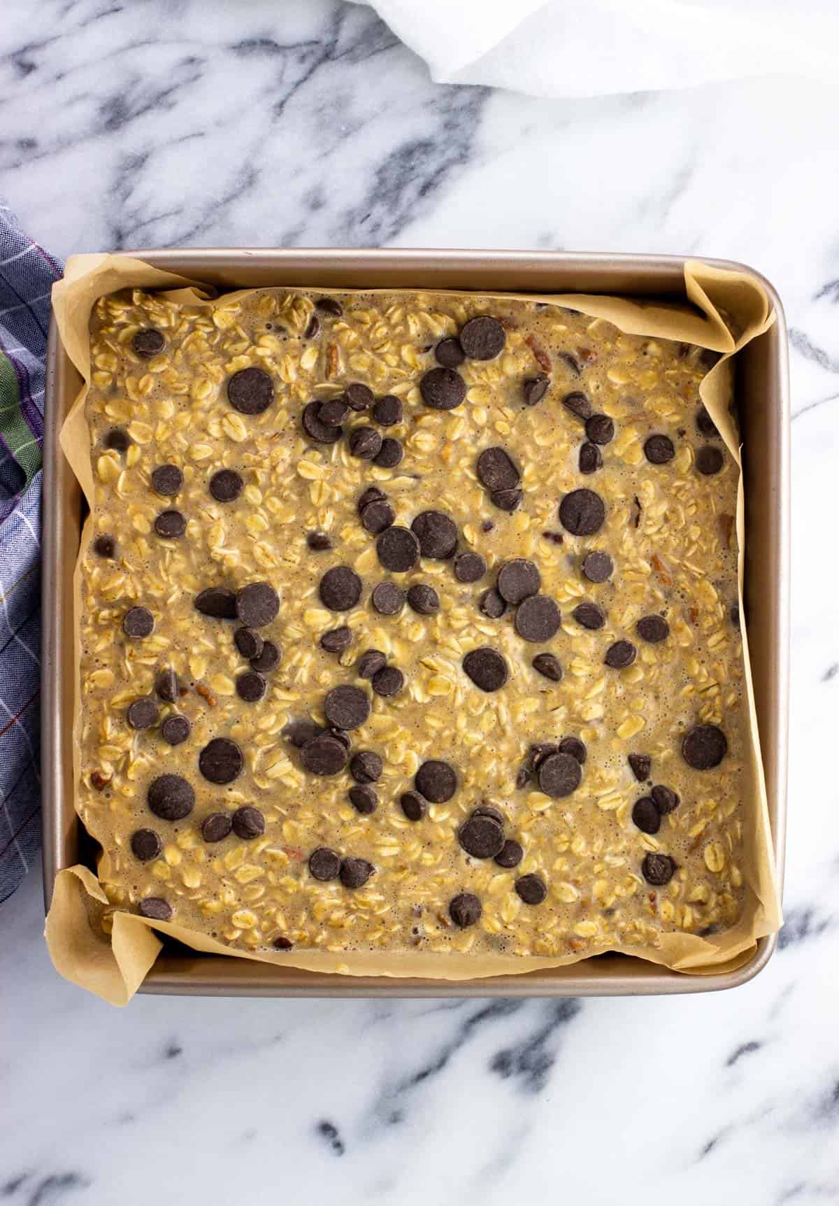 Baked oatmeal batter poured into a pan and topped with more chocolate chips.