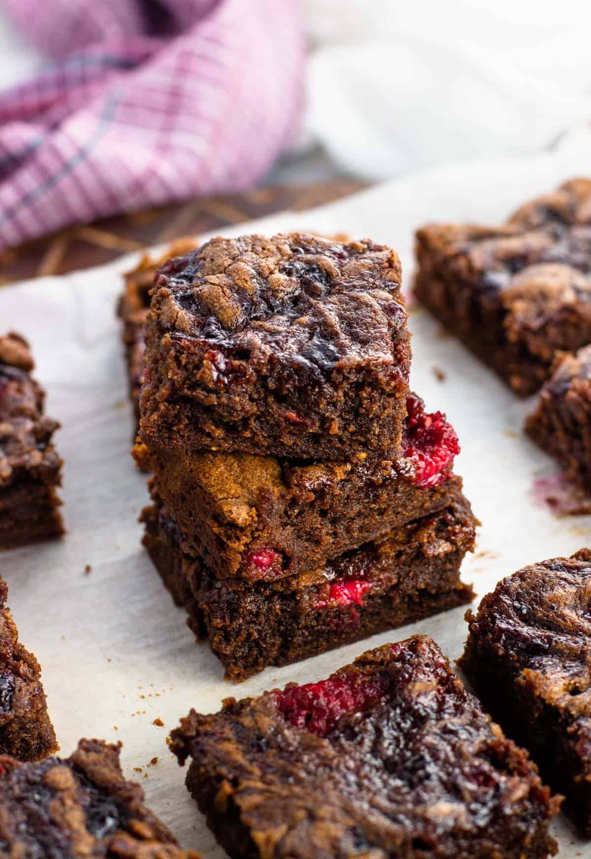 A stack of three raspberry brownies on a board.