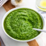 A small bowl of basil pesto with a spoon in it.