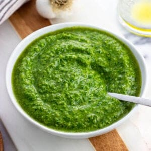 A small bowl of basil pesto with a spoon in it.