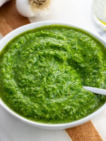 A small bowl of basil pesto with a spoon in it.