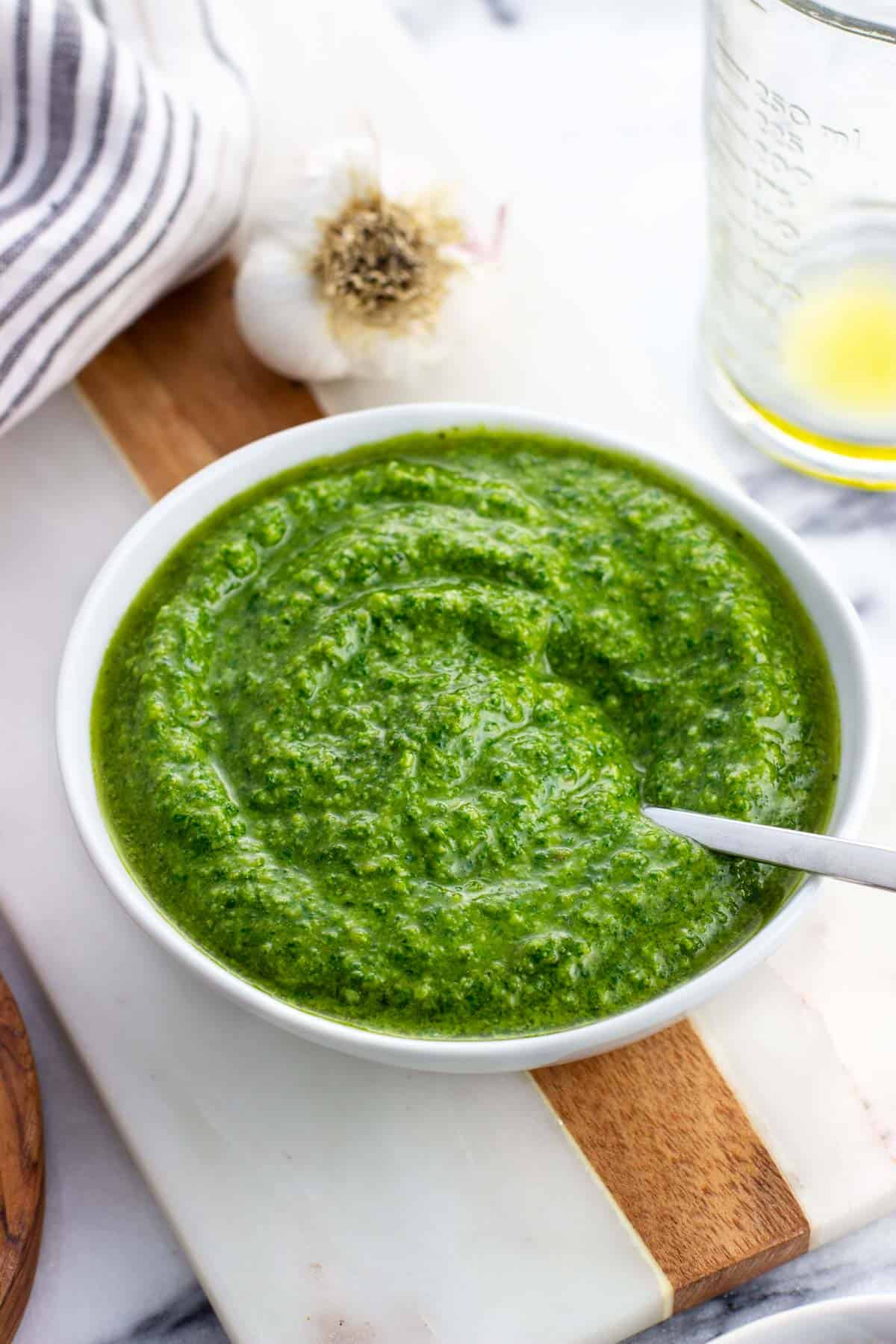 A small bowl of basil pesto with a spoon in it.