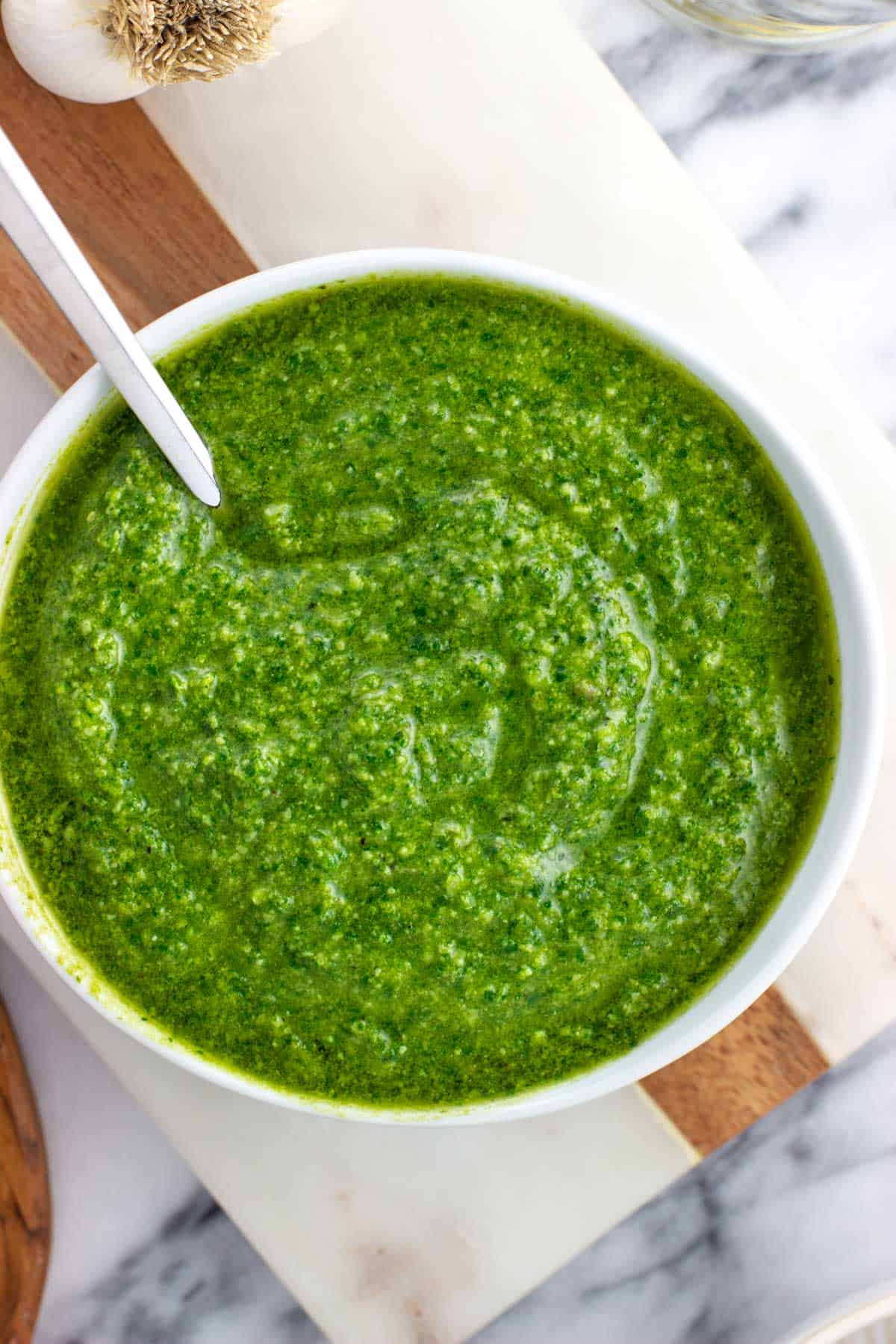 A bowl of basil pesto with a spoon in it.