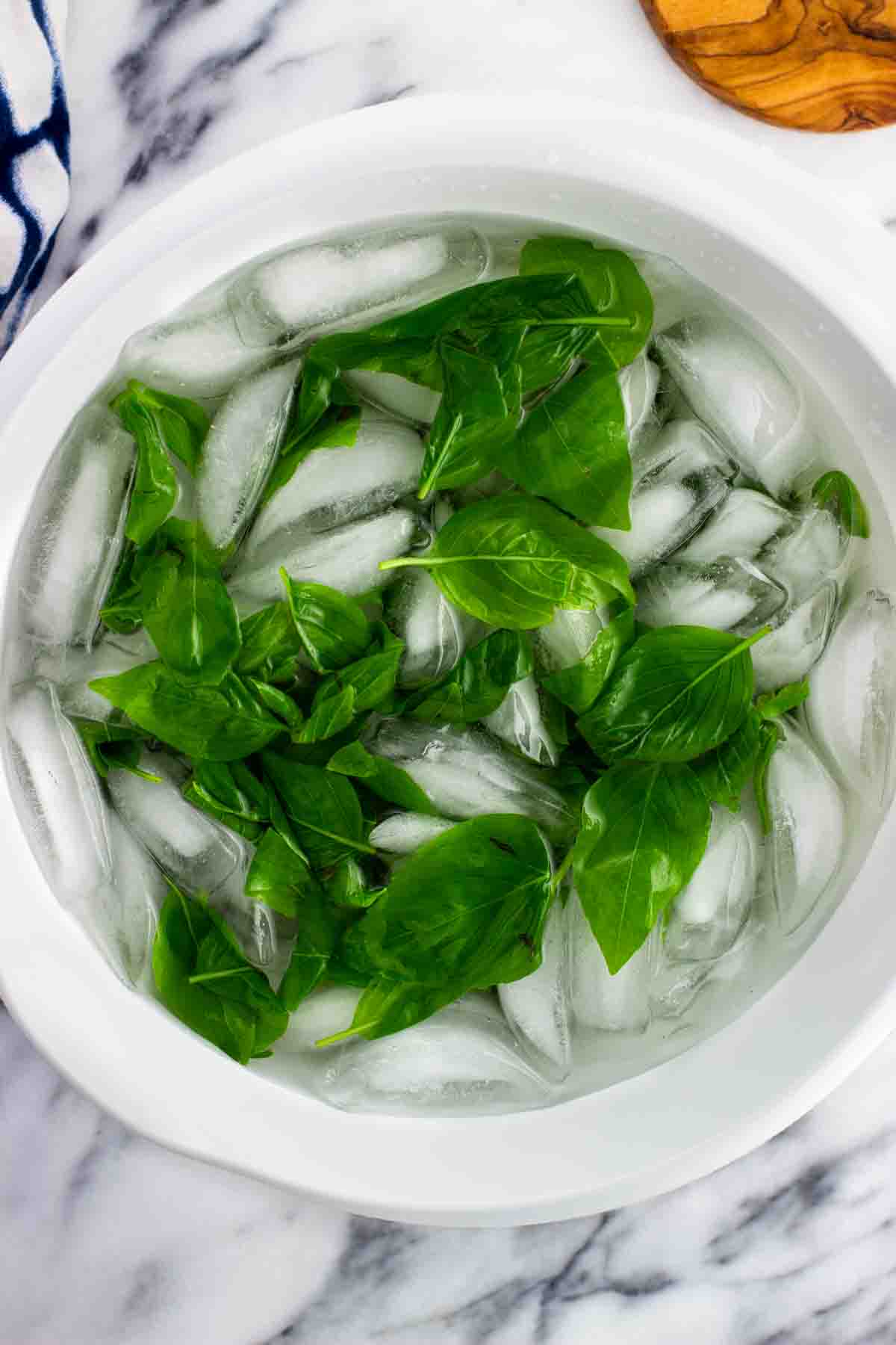 Blanched basil leaves in a large bowl of ice water.