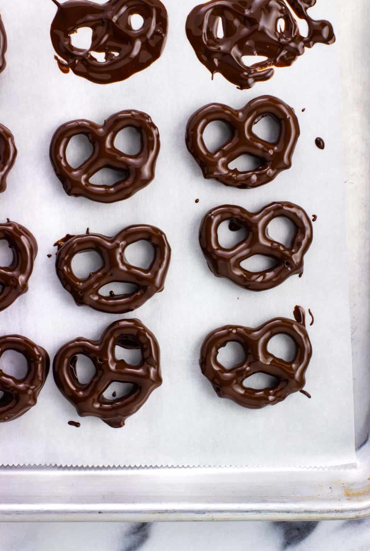 Dipped chocolate peppermint pretzels drying on a sheet of parchment paper.
