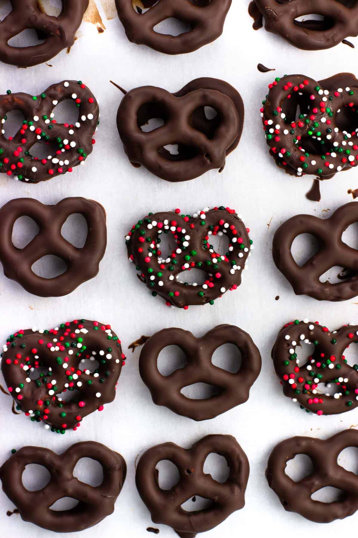 Hardened dark chocolate peppermint pretzels on a pan, some decorated in Christmas nonpareils.