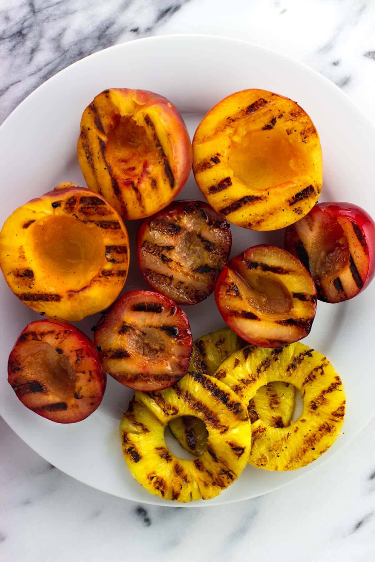 Grilled peach and plum halves on a plate.
