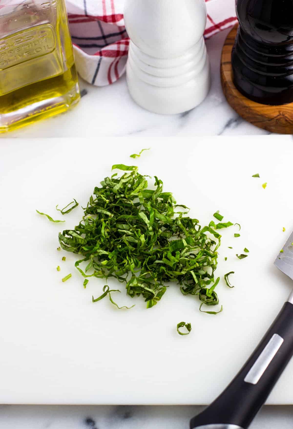 A pile of chiffonade cut basil leaves on a cutting board.