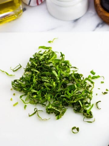 A pile of chiffonade cut basil on a cutting board.